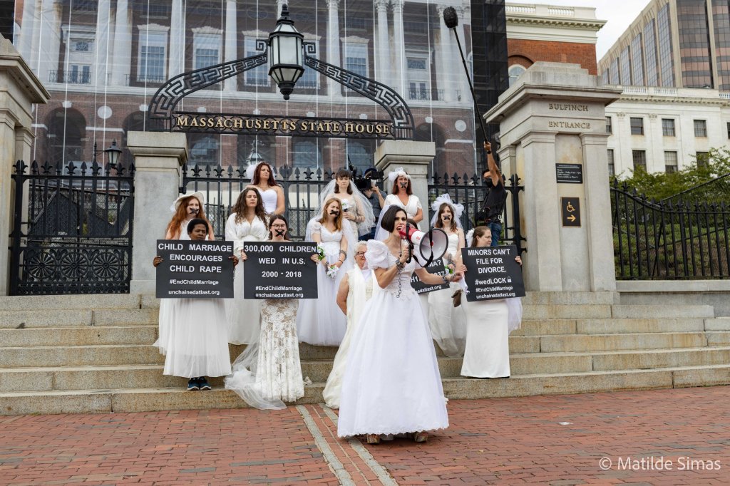 Members of the National Coalition to End Child Marriage participate in a Chain-In protest outside the Massachusetts state house. They're dressed in bridal gowns and veils with chains around their wrists and a black X taped over their mouths. Some hold signs with statistics about child marriage in the U.S. Photo credit: Mattie Simas, Capture Humanity